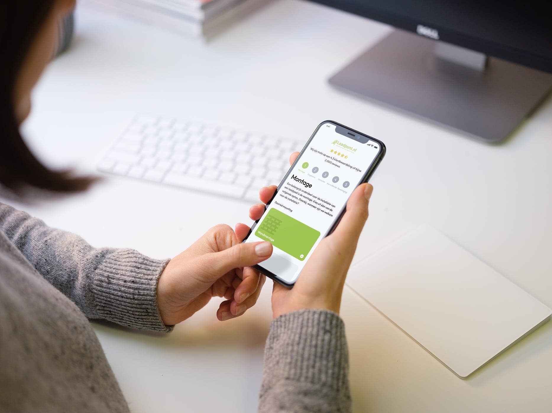 Someone going through the configurator's mounting step on a phone, with a keyboard and monitor in the background.
