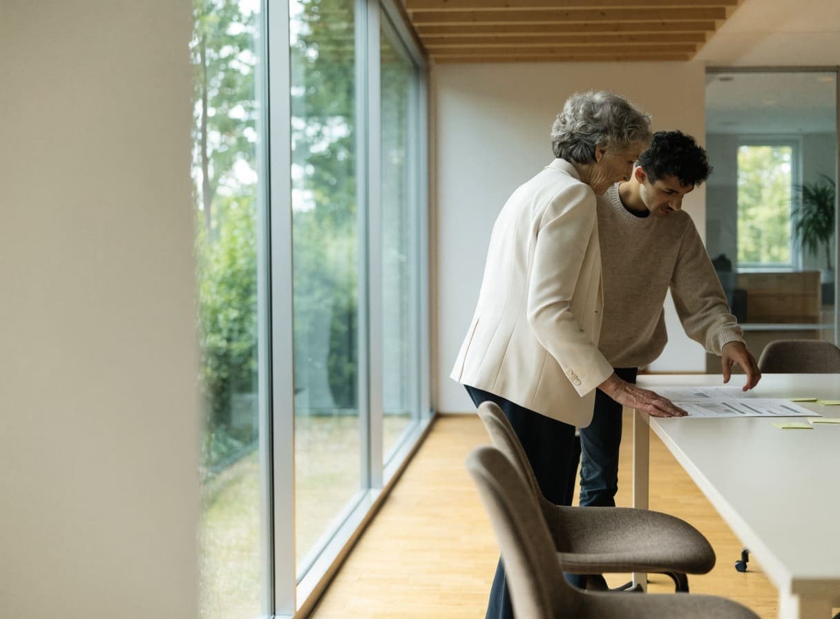 Two colleagues standing at a table by the window, looking at an overview laid out on it