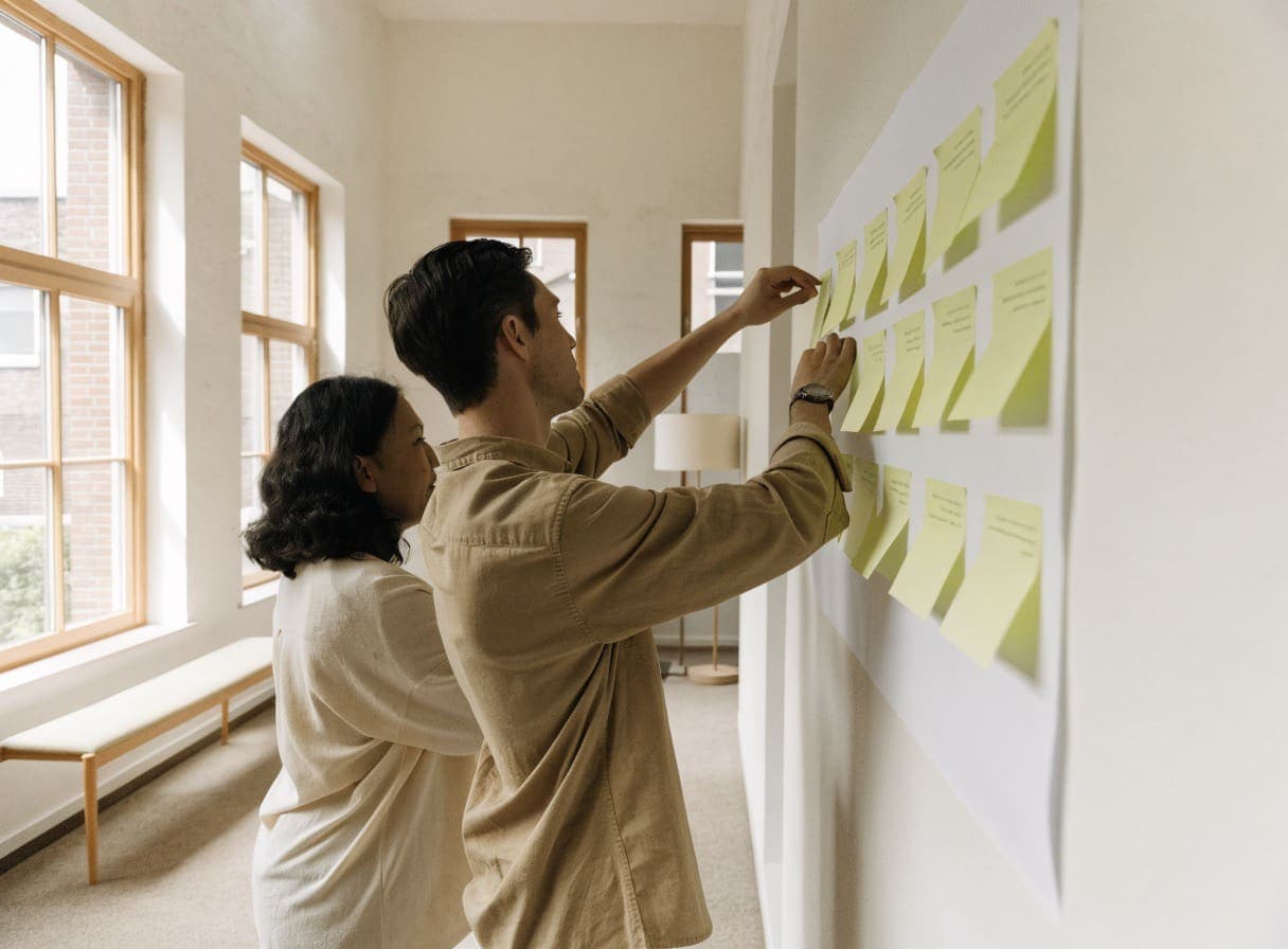 Two colleagues sticking yellow notes onto a large sheet of paper on the wall