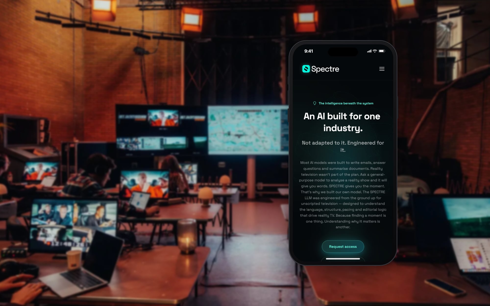 The Spectre website on a phone, in front of a production room full of screens