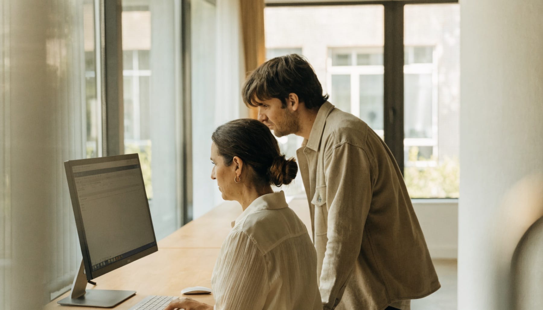 A coordinator works in an internal portal while a colleague looks on