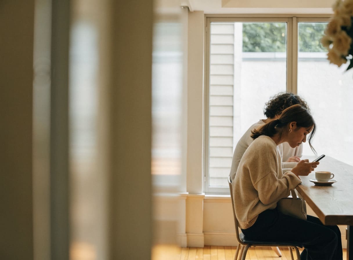 A woman orders something on her phone at a table by the window
